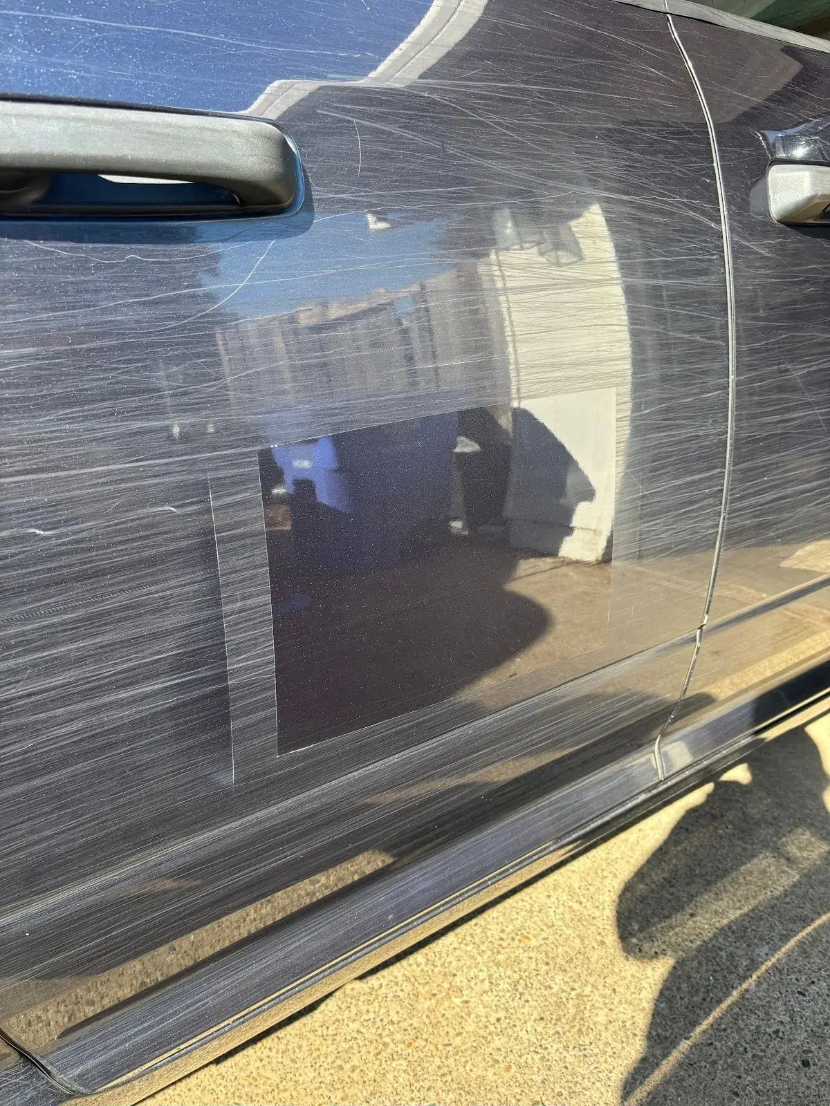 Swirl marks and scratches in black paint under sunlight with one polished square